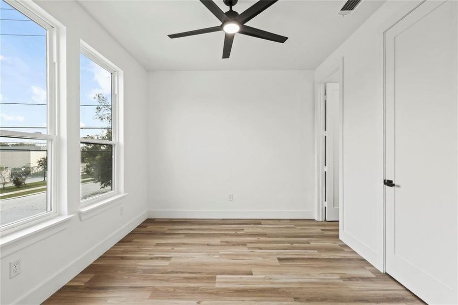 Room featuring wood-finish flooring, two large windows with white trim, a modern black ceiling fan with integrated lighting, white walls, and a white interior door with black hardware