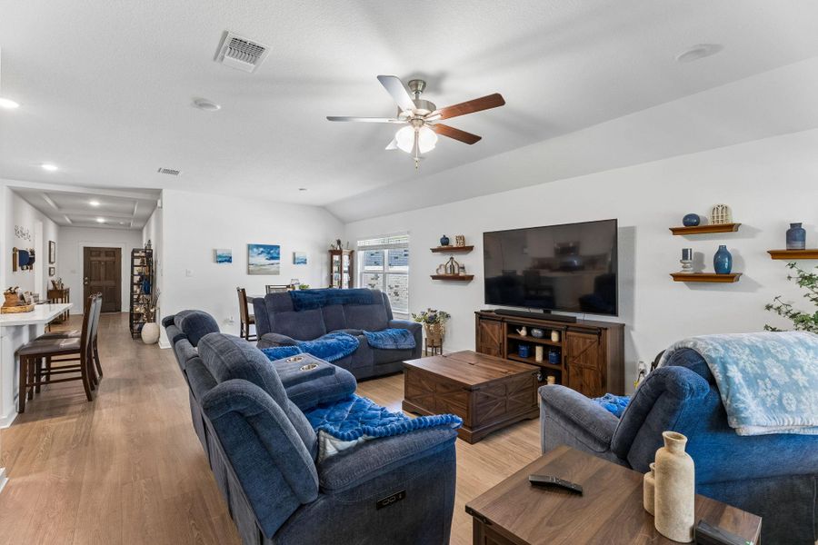 Spacious living area featuring wood-finish flooring, a vaulted ceiling, and recessed lighting