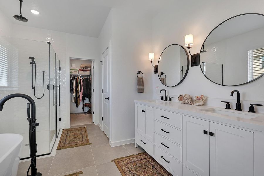 Primary Ensuite. This modern bathroom features a spacious glass-enclosed shower, dual sinks with elegant black fixtures, large circular mirrors, and ample storage. The neutral palette and soft lighting create a serene atmosphere, with a convenient walk-in closet.