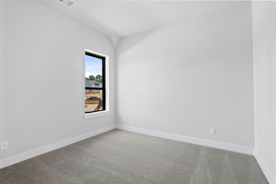 The ideal setup for multi-generational living or extended stays, this first-floor bedroom includes its own dedicated en suite bath, ensuring privacy for all. It features sloped ceilings, large window, plush carpet flooring, and neutral-toned walls.