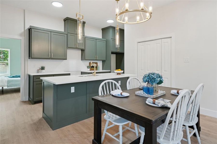 Kitchen featuring green cabinets, a chandelier, light wood finished floors, a center island with sink, and decorative light fixtures Kitchen featuring green cabinets, a chandelier, light wood finished floors, a center island with sink, and decorative light fixtures