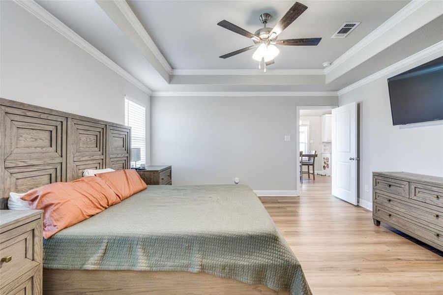 Bedroom with a raised ceiling, light wood finished floors, crown molding, and ceiling fan Bedroom with a raised ceiling, light wood finished floors, crown molding, and ceiling fan