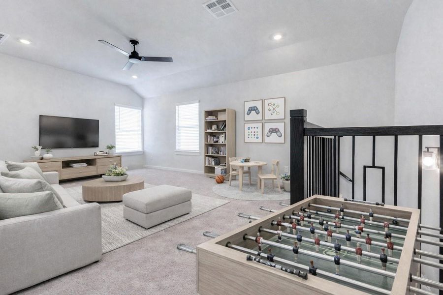 Framed by a modern black iron staircase railing, the upstairs game room is open and airy, filled with natural light from dual windows. Neutral carpeting, high ceilings, and a ceiling fan make this a perfect multi-use space for living, lounging, or working from home. This photo has been virtually staged for visual reference.