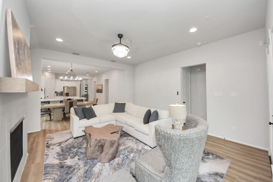 This photo showcases a modern, open-concept living room with a cozy L-shaped sofa, stylish lighting, and a natural wood coffee table. The space seamlessly connects to a dining area and kitchen, featuring light wood flooring and a neutral color palette, creating a warm and inviting atmosphere.