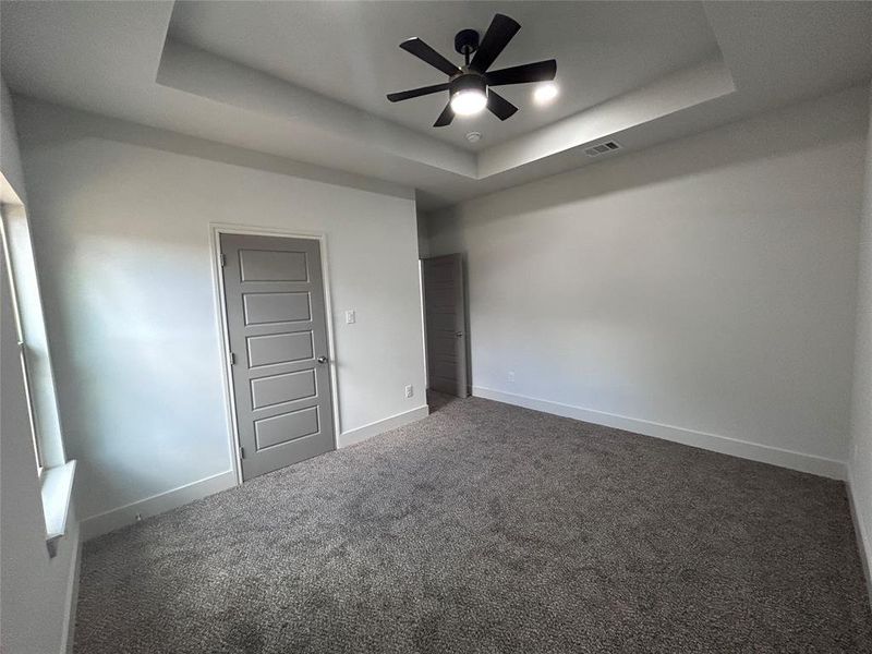 Bedroom with a raised ceiling, carpet, and ceiling fan Bedroom with a raised ceiling, carpet, and ceiling fan