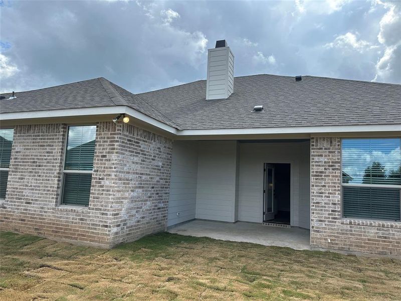 Rear exterior featuring a covered patio, brick and horizontal siding finishes, double-pane windows with blinds, and a shingle roof