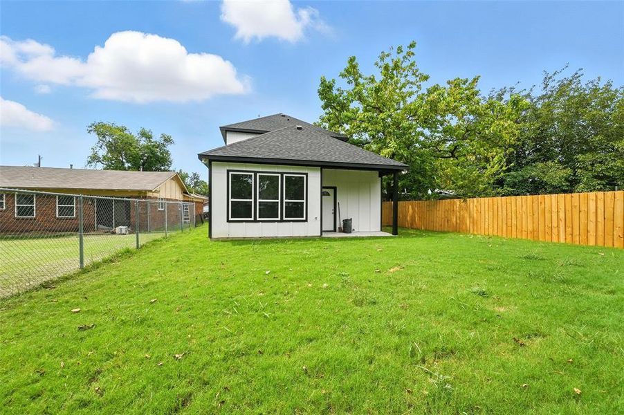 Rear view of house with a patio, roof with shingles, a fenced backyard, and board and batten siding