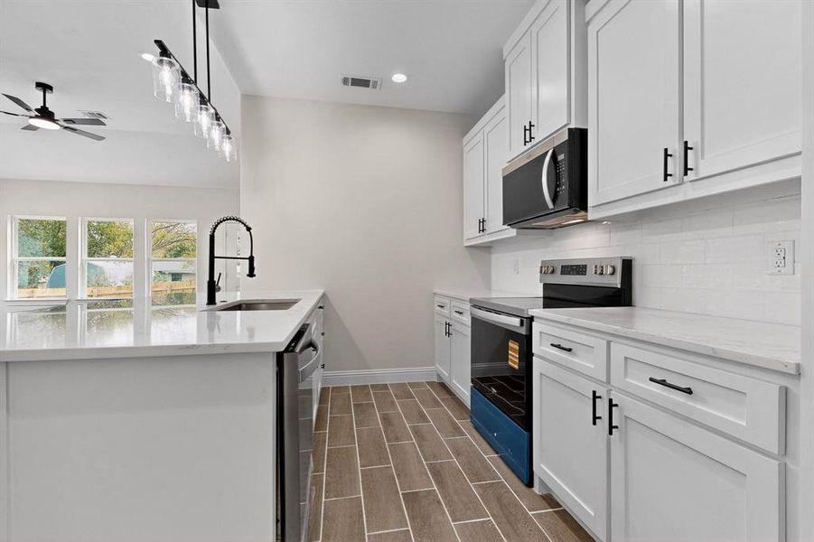 Kitchen featuring stainless steel appliances, white cabinetry, light stone countertops, hanging light fixtures, and wood tiled floors Kitchen featuring stainless steel appliances, white cabinetry, light stone countertops, hanging light fixtures, and wood tiled floors