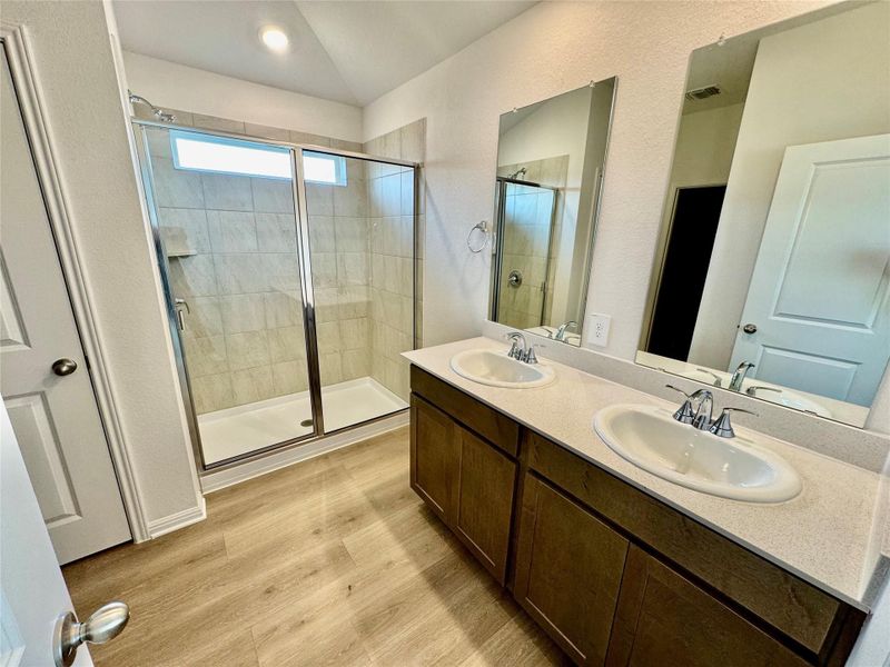 Full bath featuring a stall shower, wood finished floors, double vanity, a textured wall, and lofted ceiling