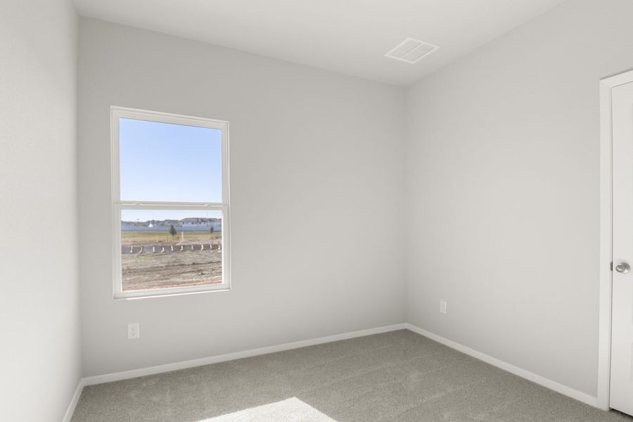Image of a bedroom with tan carpeting, light grey walls, and a window
