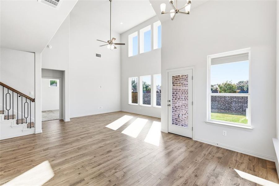 Unfurnished living room with plenty of natural light, ceiling fan, a chandelier, light wood-type flooring, and a high ceiling