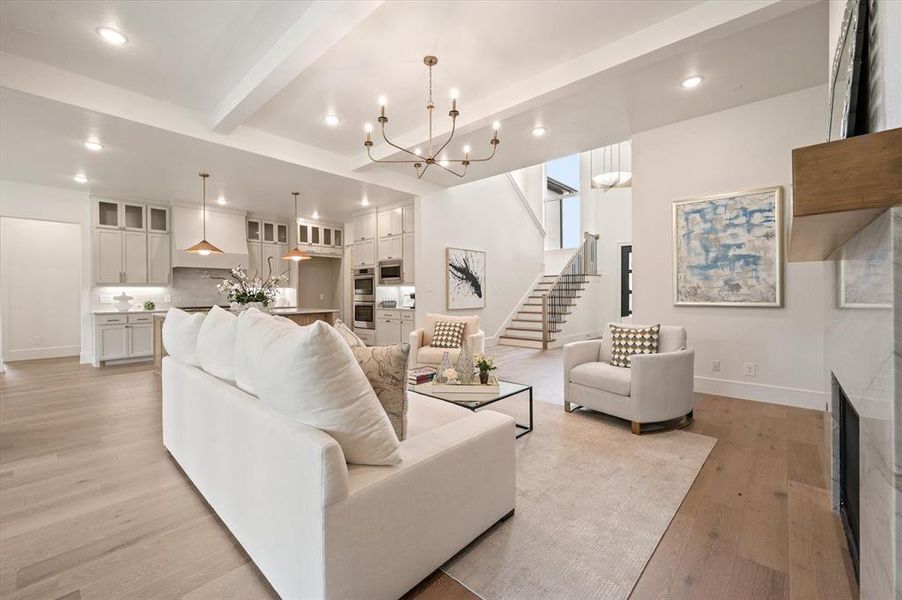 Living room with beamed ceiling, a high end fireplace, light wood-type flooring, and a chandelier