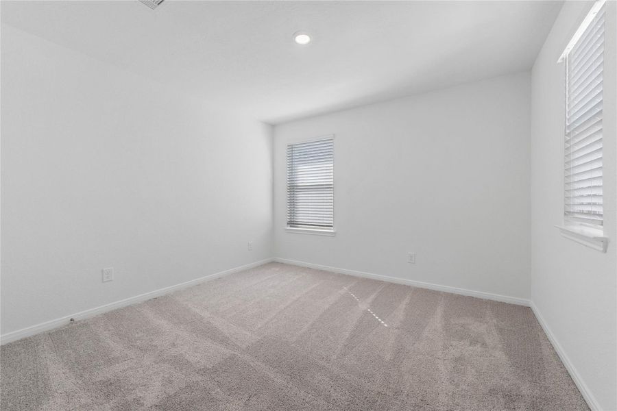 This secondary bedroom offers comfort and style with plush carpeting, neutral paint tones, recessed lighting, large window with blinds, and a generously sized closet.