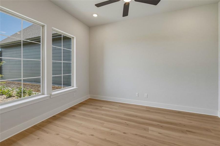 Room with wood-finish flooring, two large windows with grid patterns, a ceiling fan, and recessed lighting Room with wood-finish flooring, two large windows with grid patterns, a ceiling fan, and recessed lighting