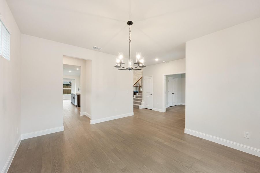 Empty dining room with hardwood floors, chandelier, and open view to kitchen and staircase Empty dining room with hardwood floors, chandelier, and open view to kitchen and staircase