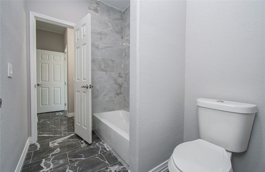 This bathroom features modern gray tiles, a bathtub-shower combo, and a sleek toilet. The space is bright with clean lines and white accents, creating a fresh and inviting atmosphere.
