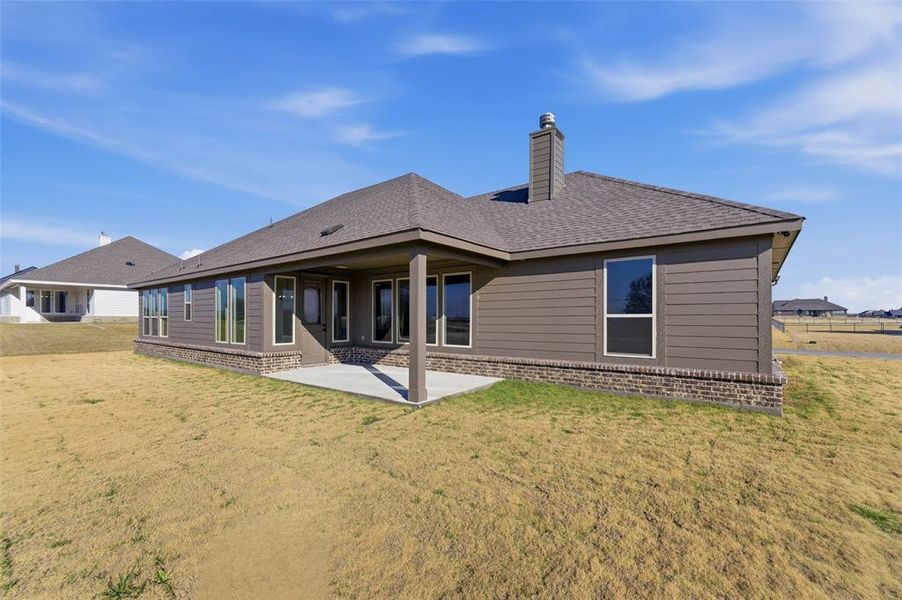 Rear view of house with a patio area, brick siding, roof with shingles, and a yard