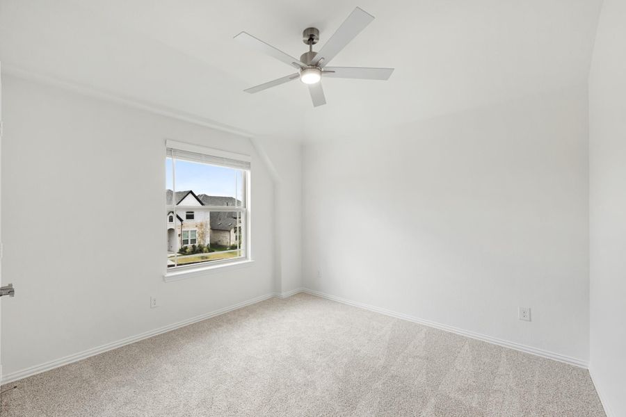 Empty bedroom with carpet flooring, ceiling fan, vaulted ceiling, and single window with neighborhood view