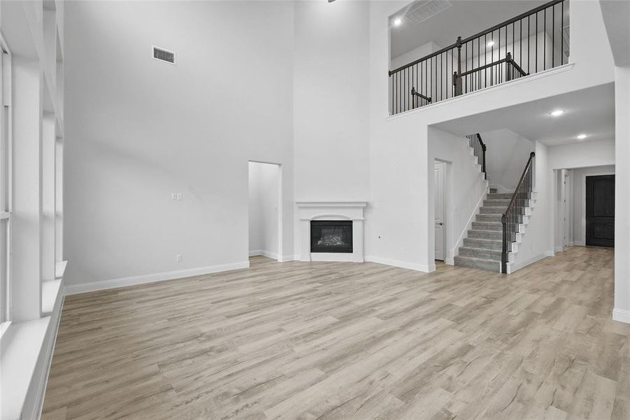 Unfurnished living room with a towering ceiling, stairway, light wood-type flooring, and baseboards