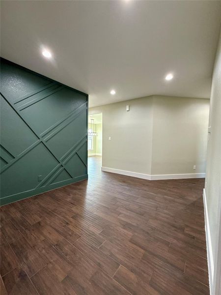 This photo shows a hallway with dark wood tile flooring and a modern accent wall in rich green. The recessed lighting adds a bright, welcoming feel. The space leads into another room, suggesting an open floor plan. This photo shows a hallway with dark wood tile flooring and a modern accent wall in rich green. The recessed lighting adds a bright, welcoming feel. The space leads into another room, suggesting an open floor plan.