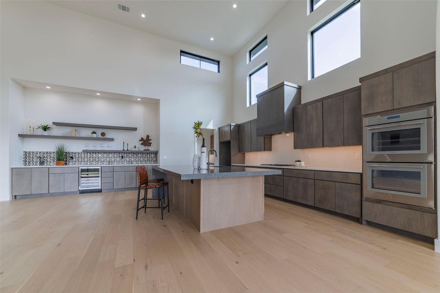 Kitchen featuring modern cabinets, open shelves, a kitchen breakfast bar, stainless steel double oven, and a high ceiling
