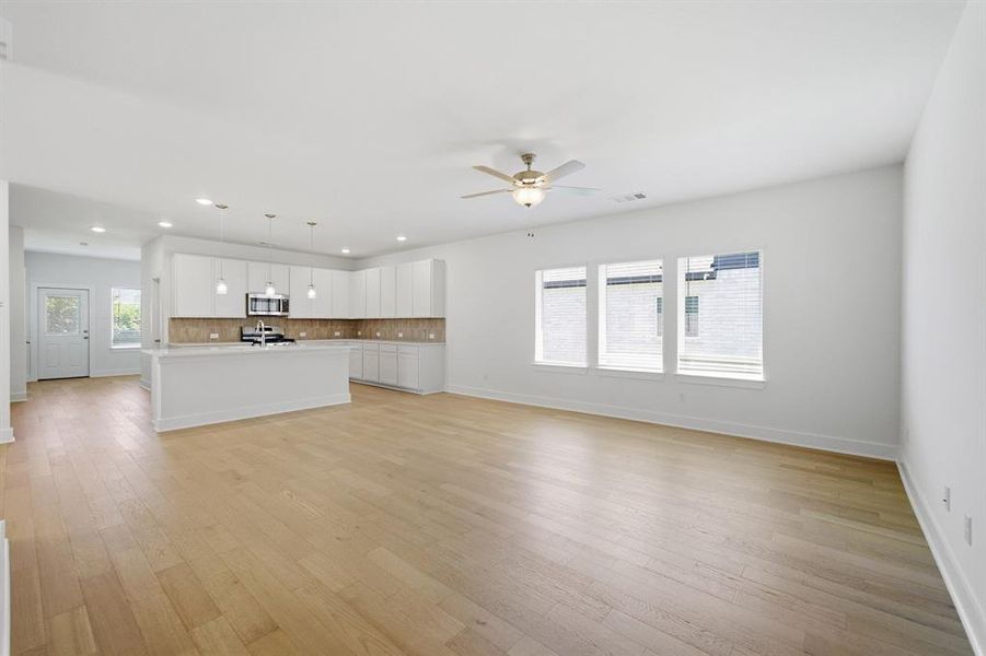 Open-concept living space featuring wood-finish flooring, a contemporary kitchen island with pendant lighting, white cabinetry, and stainless steel appliances