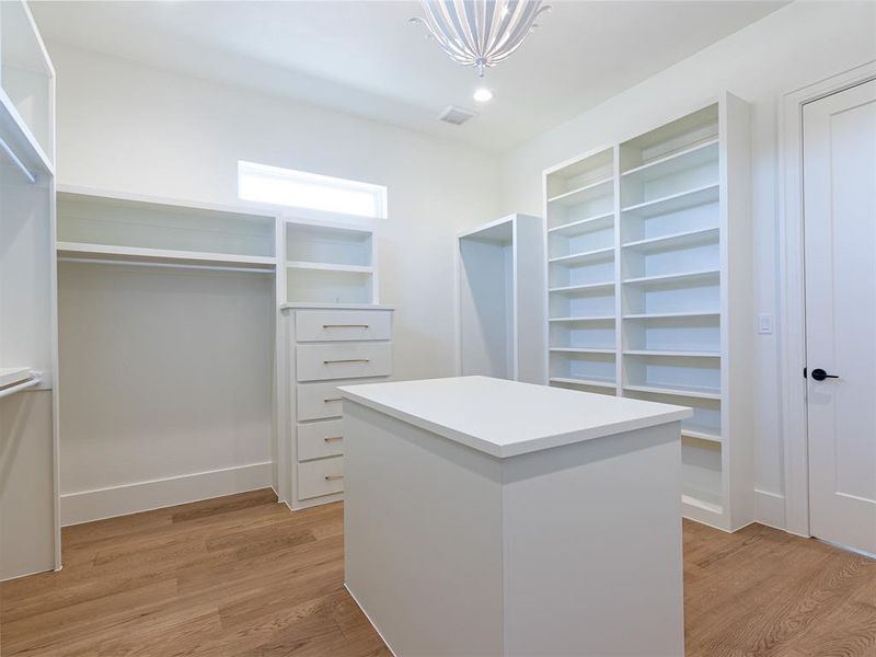 Primary walk-in closet features lots of built-in cabinets and wood flooring.