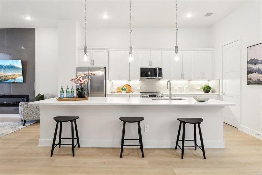 Kitchen featuring a large island, stainless steel appliances, light wood-type flooring, white cabinetry, and a sink