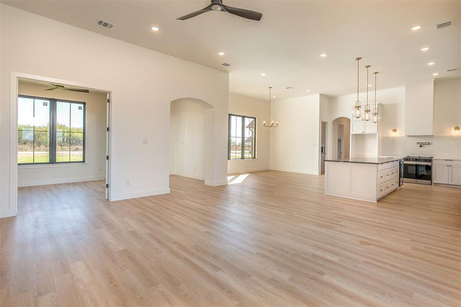 Unfurnished living room with ceiling fan with notable chandelier, light wood-type flooring, and a healthy amount of sunlight