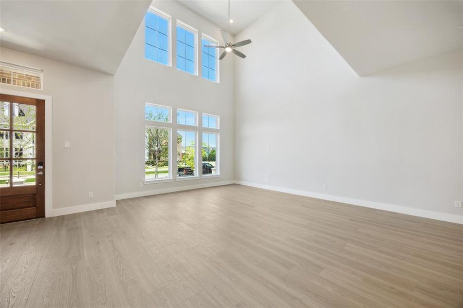 Unfurnished living room featuring light wood finished floors, a towering ceiling, and a ceiling fan