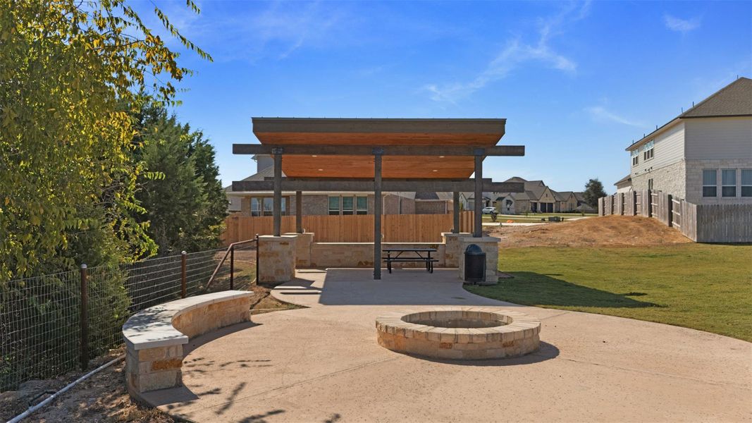 Outdoor gathering area featuring a stone fire pit, curved stone seating, and a covered patio with a picnic table Outdoor gathering area featuring a stone fire pit, curved stone seating, and a covered patio with a picnic table