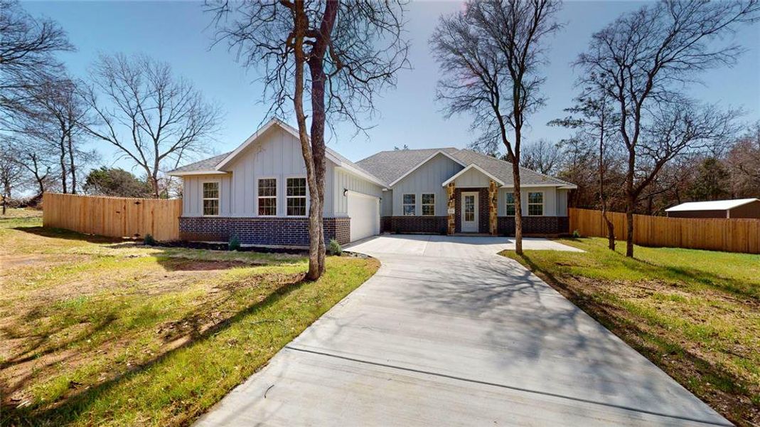 View of front of property with board and batten siding, brick siding, driveway, and fence