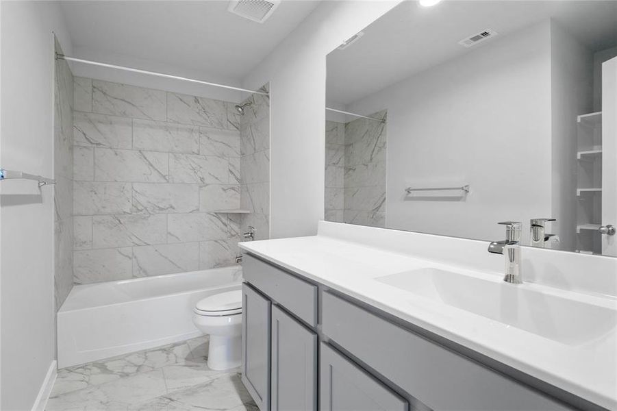 Secondary bath features tile flooring, bath/shower combo with tile surround, light wood cabinets, beautiful light countertops, mirror, sleek fixtures and modern finishes!