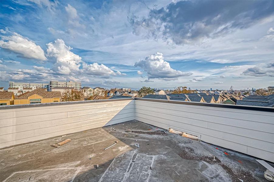 This photo showcases a spacious rooftop deck with a panoramic view of the neighborhood, perfect for relaxing or entertaining. The sky is clear with beautiful clouds, adding to the serene atmosphere.