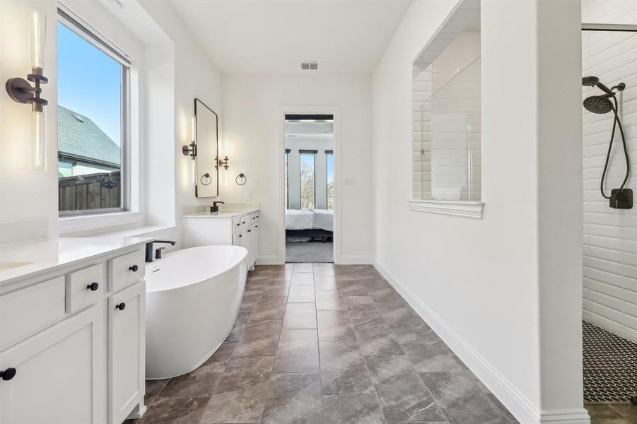 Ensuite bathroom featuring a tile shower, visible vents, ensuite bathroom, vanity, and a freestanding bath Ensuite bathroom featuring a tile shower, visible vents, ensuite bathroom, vanity, and a freestanding bath