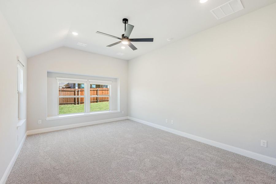 Empty bedroom with vaulted ceiling, ceiling fan, carpet flooring, and backyard-facing window Empty bedroom with vaulted ceiling, ceiling fan, carpet flooring, and backyard-facing window
