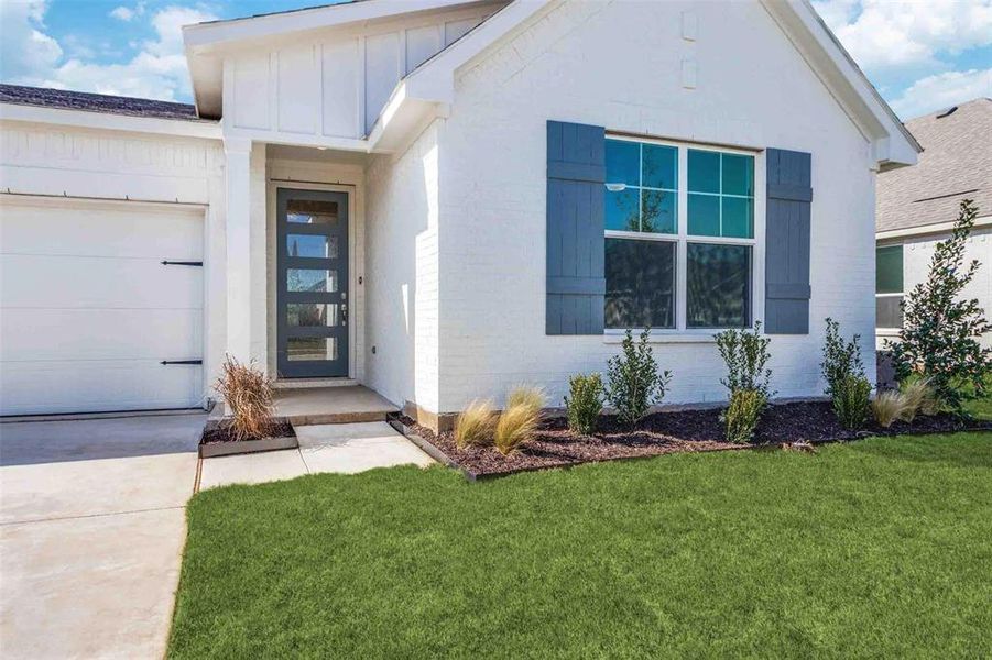 Entrance to property featuring a lawn, board and batten siding, brick siding, and a garage