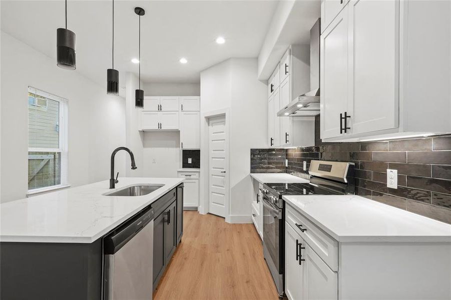 Kitchen featuring appliances with stainless steel finishes, wall chimney range hood, sink, pendant lighting, and white cabinets