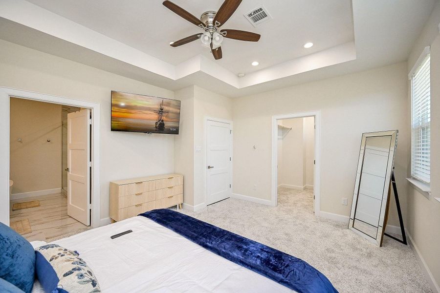 Serene primary bedroom featuring tray ceilings, abundant natural light, and modern comfort.