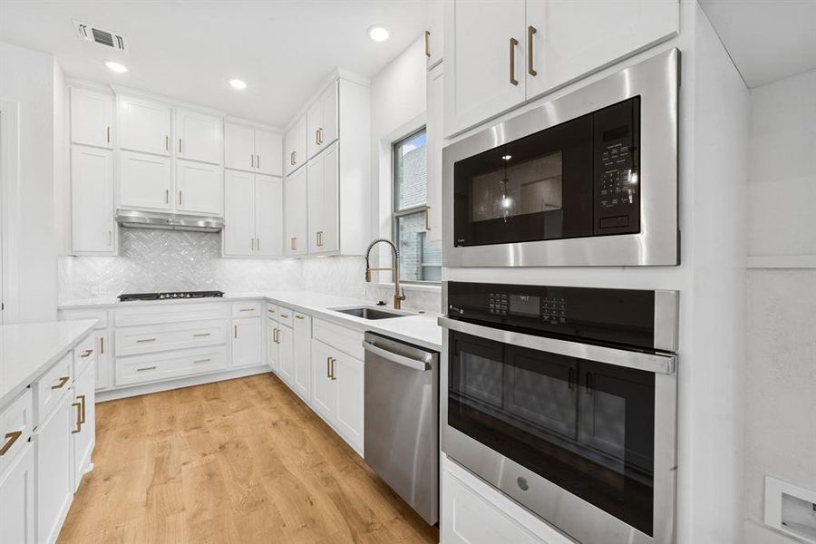 Kitchen featuring stainless steel appliances, white cabinets, light wood-style flooring, backsplash, and light stone countertops Kitchen featuring stainless steel appliances, white cabinets, light wood-style flooring, backsplash, and light stone countertops