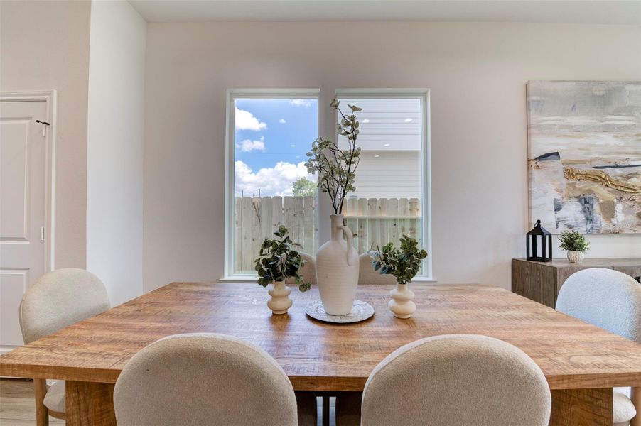 Dining area with hardwood floors, dual windows overlooking backyard, and open sightline to living room and kitchen.