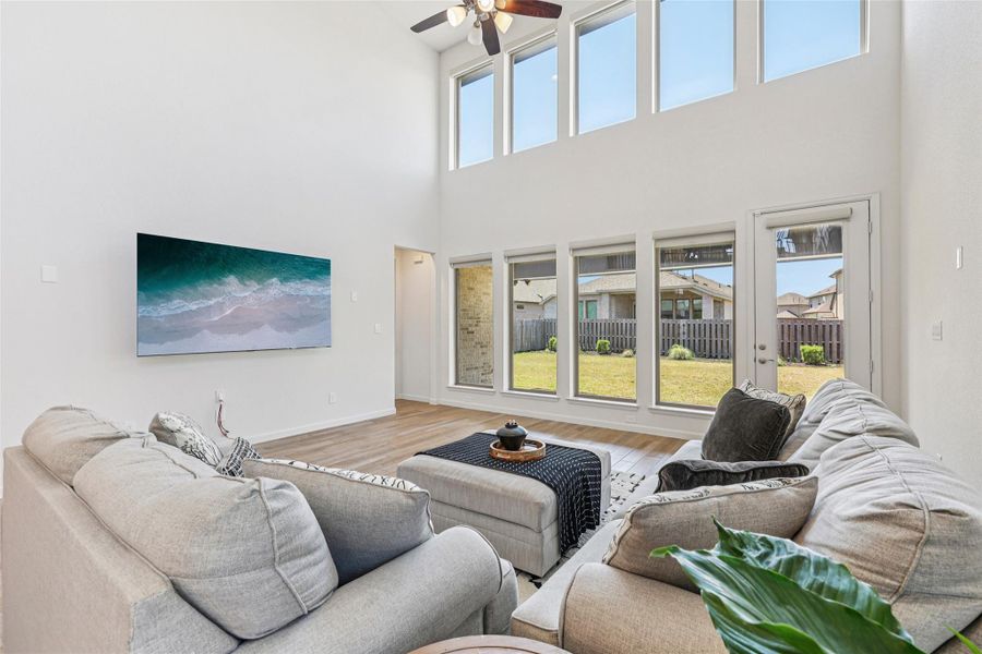 The living room features high ceilings with a ceiling fan, large windows providing natural light, and light-toned flooring