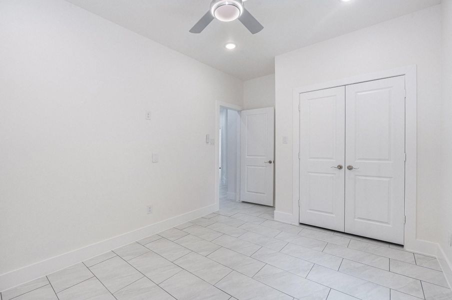 This photo showcases a bright, modern room with tiled flooring, a ceiling fan, and a double-door closet. The neutral color palette and recessed lighting add to the spacious feel, suitable for a bedroom or office. This photo showcases a bright, modern room with tiled flooring, a ceiling fan, and a double-door closet. The neutral color palette and recessed lighting add to the spacious feel, suitable for a bedroom or office.