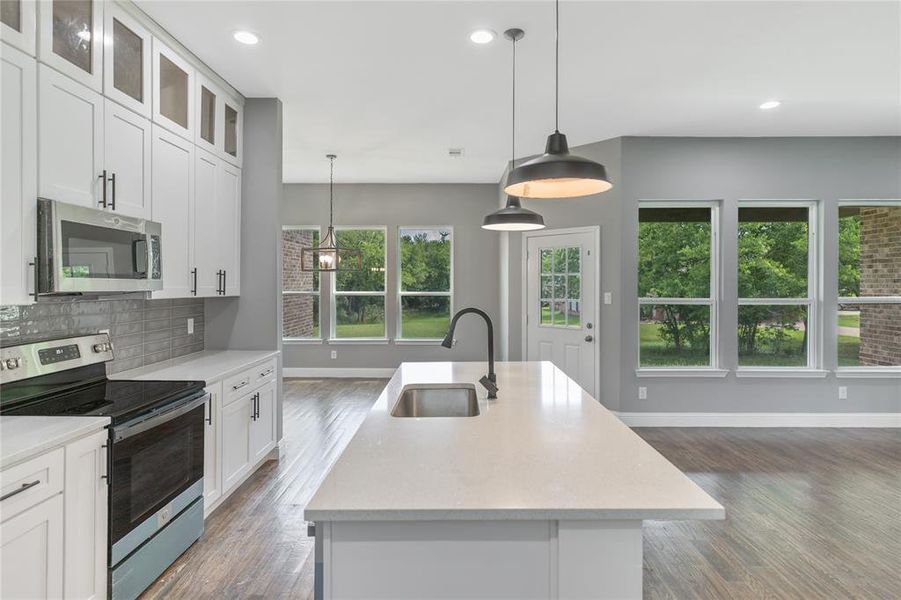 Kitchen with appliances with stainless steel finishes, an island with sink, white cabinets, light stone counters, and tasteful backsplash Kitchen with appliances with stainless steel finishes, an island with sink, white cabinets, light stone counters, and tasteful backsplash