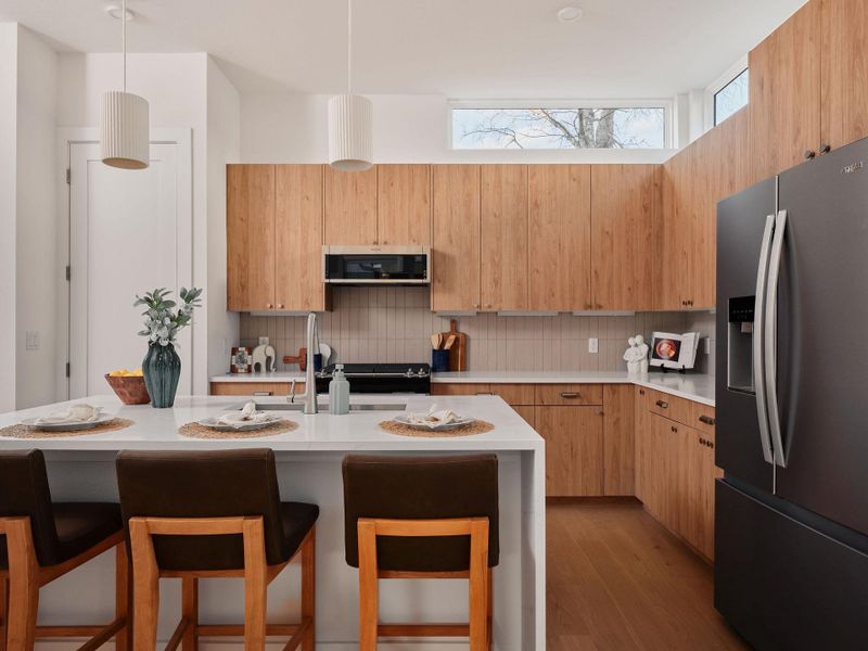 Kitchen with stainless steel refrigerator with ice dispenser, a kitchen breakfast bar, light stone countertops, and dark wood-style flooring