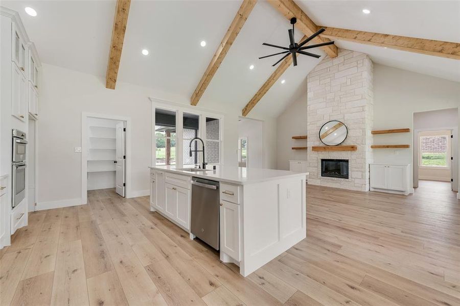 Spacious open-concept interior featuring light wood-finish flooring, vaulted ceilings with exposed wood beams, and recessed lighting