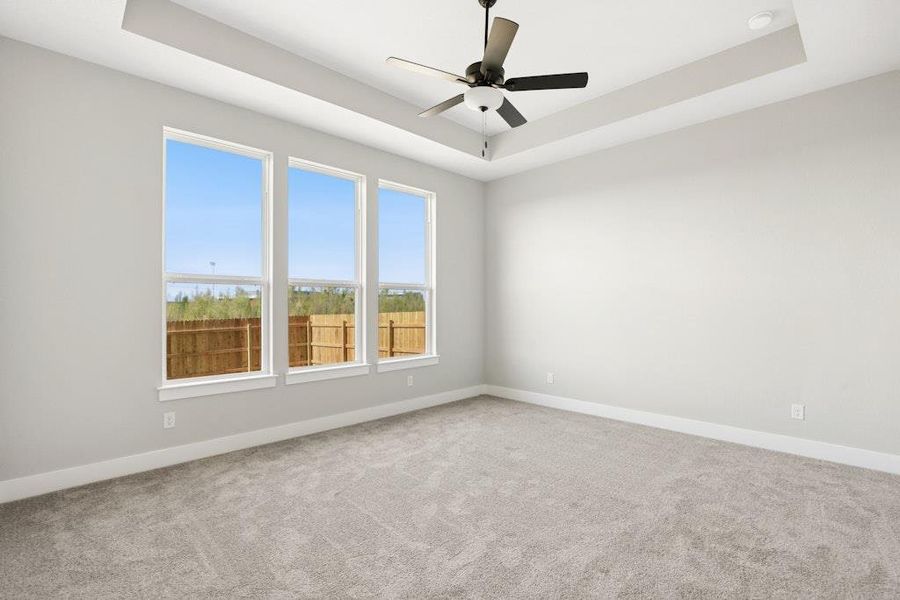 Carpeted empty room featuring a tray ceiling and a ceiling fan Carpeted empty room featuring a tray ceiling and a ceiling fan