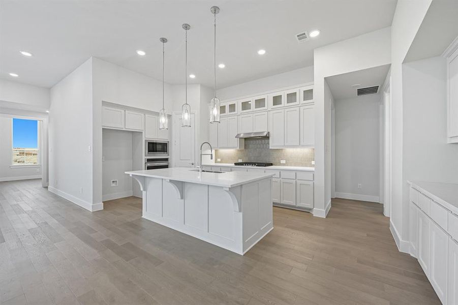 Kitchen with white cabinets, a breakfast bar, an island with sink, tasteful backsplash, and decorative light fixtures Kitchen with white cabinets, a breakfast bar, an island with sink, tasteful backsplash, and decorative light fixtures