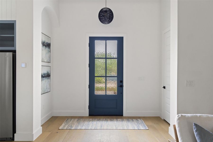 Navy blue entry door with clear glass panels, complemented by wood-finish flooring and a contemporary spherical pendant light fixture