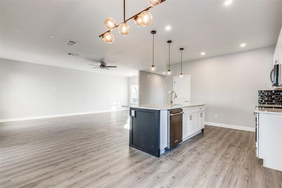 Kitchen featuring pendant lighting, ceiling fan, an island with sink, and white cabinets